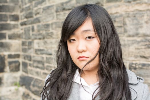 Portrait of young girl in front of a stone wall looking upset