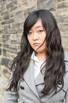 Portrait of young girl in front of a stone wall looking upset