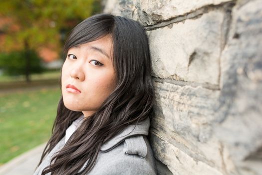 Portrait of young girl in front of a stone wall looking upset