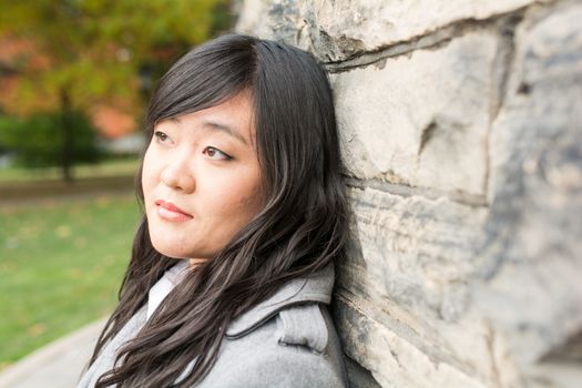 Portrait of young woman standing back against a stone wall looking hopeful