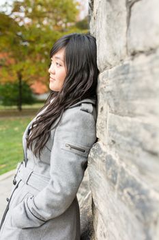 Portrait of young woman standing back against a stone wall looking hopeful