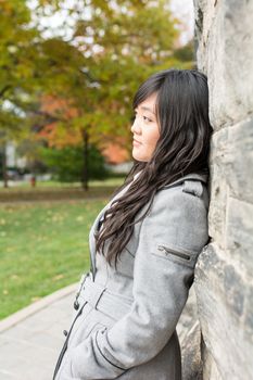 Portrait of young woman standing back against a stone wall looking hopeful