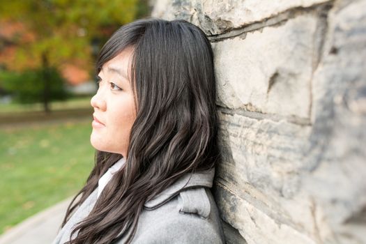 Portrait of young woman standing back against a stone wall looking hopeful