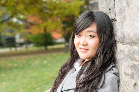 Portrait of young woman standing back against a stone wall looking innocent