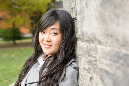 Portrait of young woman standing back against a stone wall looking innocent