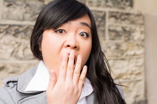 Portrait of attractive young woman looking surprised and trying to cover mouth