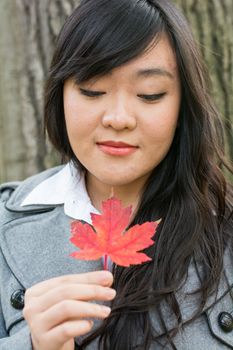 Autumn portrait of cute young woman in front of a maple tree holding a maple leaf with eyes closed