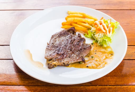 beef steak on white dish with salad french fries and pepper gravy sauce on wood table