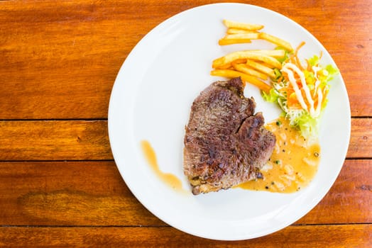 beef steak on white dish with salad french fries and pepper gravy sauce on wood table
