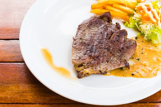 beef steak on white dish with salad french fries and pepper gravy sauce on wood table