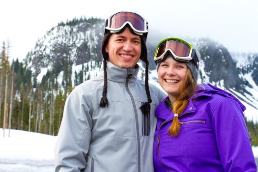 A happy couple together on the mountain resort in the snow for a day of skiing and snowboarding.