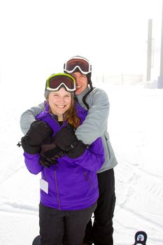 A happy couple together on the mountain resort in the snow for a day of skiing and snowboarding.