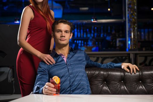 Portrait of a successful man in a nightclub, sitting on the couch, next to a woman in a red dress