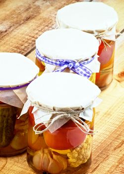 Arrangement of Homemade Pickled Vegetables in Glass Jars with Butter-paper closeup on Wooden background