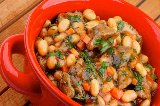 Delicious Homemade White Beans Stew with Beef and Greens in Red Pot closeup on Wooden background