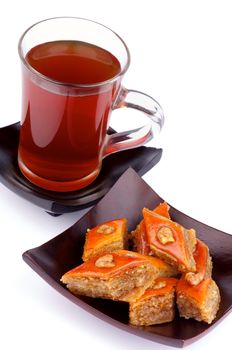 Cup of Black Tea and Arrangement of Delicious Baklava Sweets with Nuts on Black Plates isolated on white background