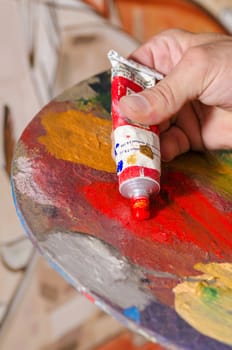 Painter squeezing red paint onto his palette