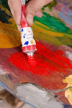 Painter squeezing red paint onto his palette