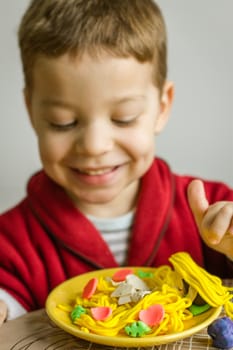 Portrait of cute child posing with his original spaghetti dish, made in colorful plasticine