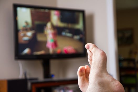 Shallow depth of field with feet in focus of a guy watching family movies on the TV in the background