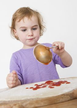 child putting sieved tomatoes on dough. studio shot in grey background