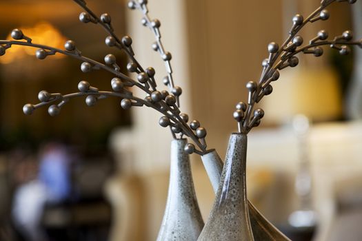 Close focus on three vases, one tilted, with graceful, round silver beads on branches in casual celebratory still life. Copy space in unfocused background.