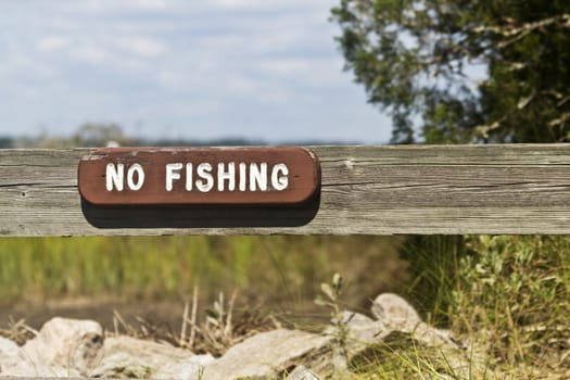 Wooden No Fishing sign with white letters on fence board is worn by time and weather; location is South Carolina, Huntingdon Beach State Park; 