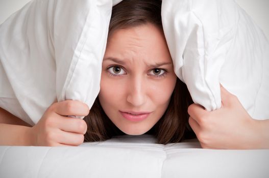 Woman with a pillow over her head, not wanting to get out of the bed, isolated in white