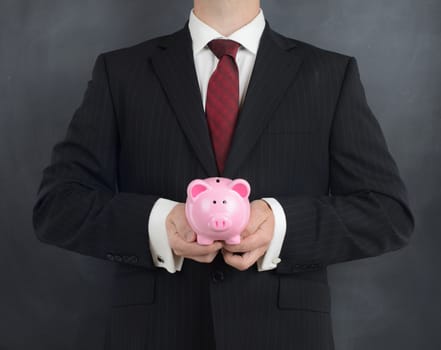 man in a suit holding a piggy bank on a grey background