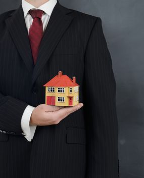 man in a suit holding a minature house concept for real estate