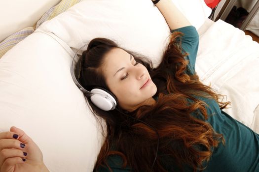 A young adult woman listening music with headphones in bed.