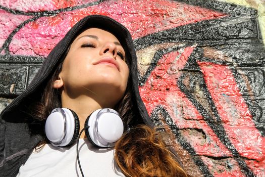 A young woman enjoying the Sunlight leaning against a wall.
