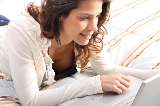 A young girl laying on the bed and surfing on the Internet with a Laptop.