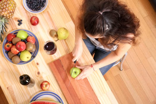 A young adult woman cutting fruits in the kitchen.