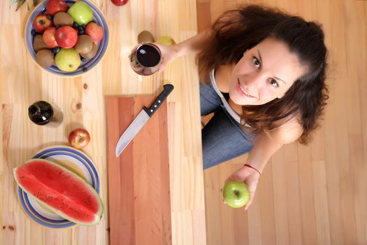 A young adult woman with fruits and wine in the kitchen.