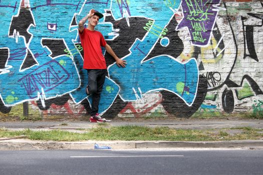 A greeting young Rapper greeting in front of a Graffiti wall.