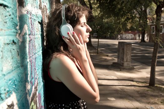 A vintage dressed girl listing to music in a urban environment.