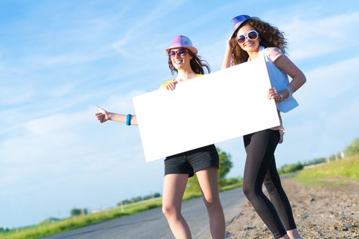 Two young women stand with a blank banner on the side of the road, place for text