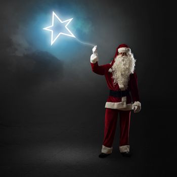 Santa Claus is holding a shining star sign on a string