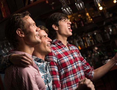 Three men stand in a row embracing smile and look in front of you, sports fans