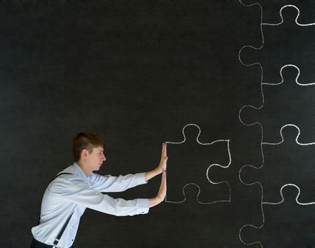 Sales businessman pushing chalk jigsaw puzzle piece into place on blackboard background