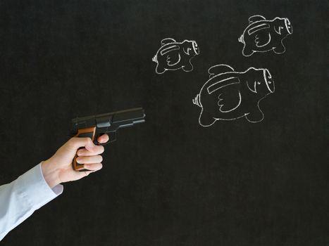 Businessman shooting gun at flying money piggy banks in chalk on blackboard background