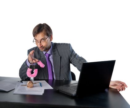 young businessman at his desk offers pink handcuffs