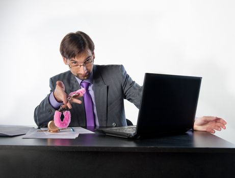 young businessman at his desk offers pink handcuffs