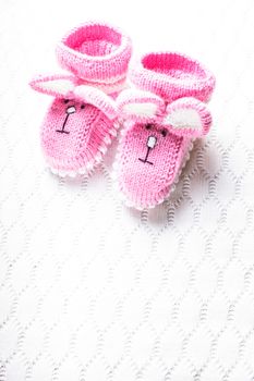 Knitted pink baby booties with rabbit muzzle over textile background