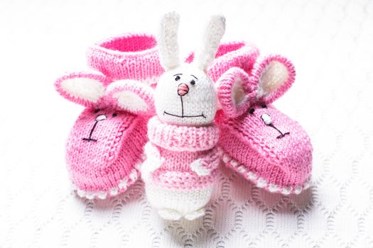 Knitted pink baby booties with rabbit muzzle and toy over textile background