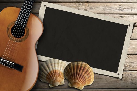 Acoustic brown guitar and aged photo frame with two sea shells on beach wooden floor over summer sand