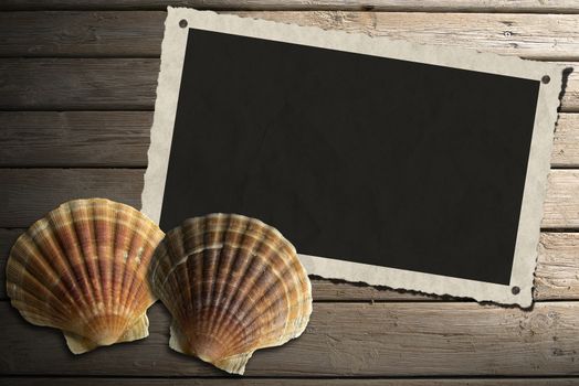 Aged photo frame with two sea shells on beach wooden floor over summer sand