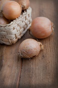 Onions in a rustic woven straw basket with two lying alongside on the wooden table, high angle view