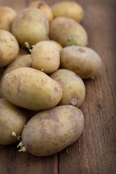 Pile of fresh raw potatoes on a wooden table, vertical format with shallow dof